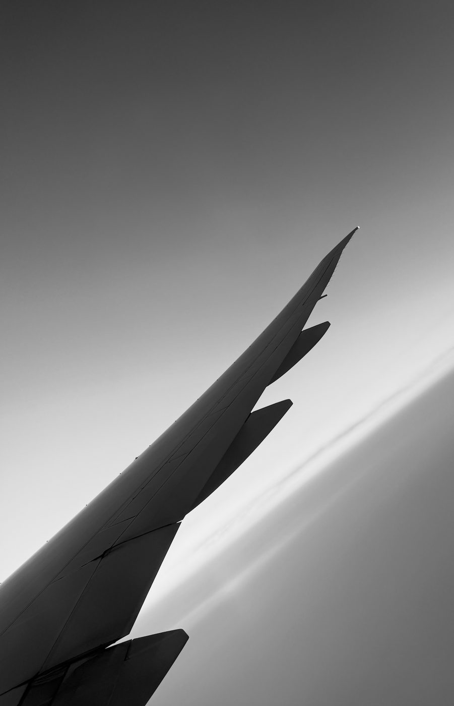 An aircraft wing angled against a gradient sky, in black and white